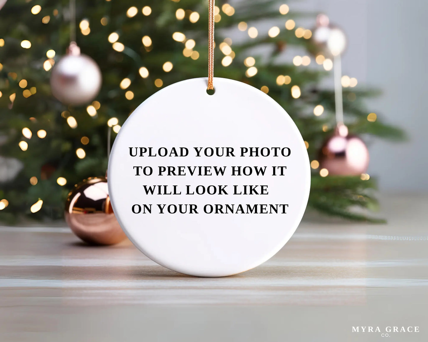 A white ornament with text on it, placed in front of a blurred Christmas tree with ornaments.